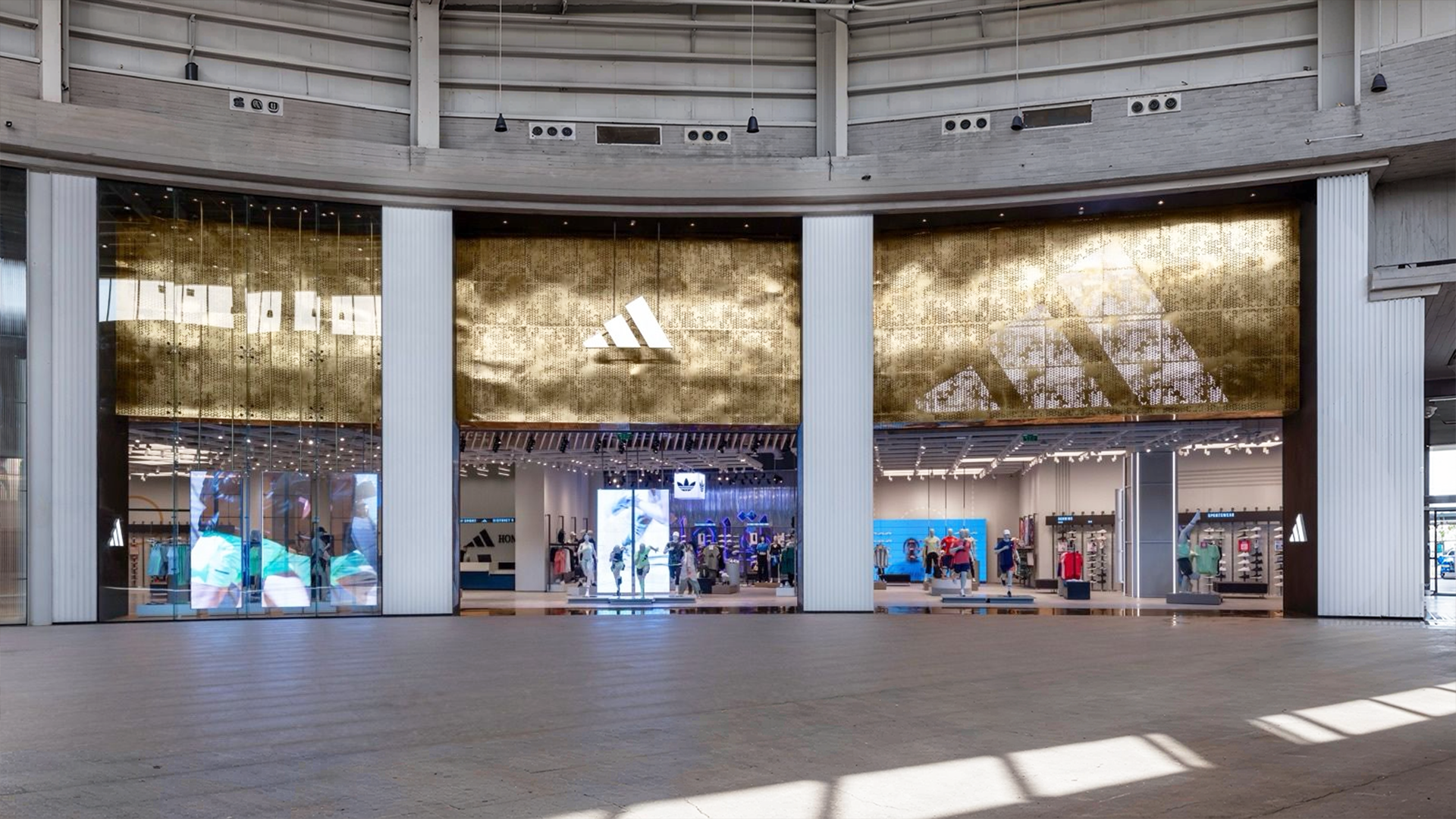 Modern Adidas District 5 retail store interior featuring a grand double-height ceiling, industrial steel fixtures, and an expansive athletic footwear wall